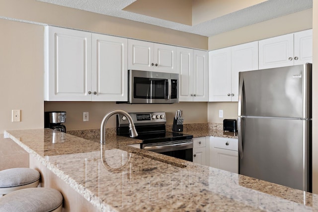 kitchen with stainless steel appliances, white cabinetry, a kitchen breakfast bar, and light stone countertops