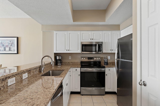 kitchen with light tile patterned floors, light stone counters, stainless steel appliances, a sink, and white cabinets