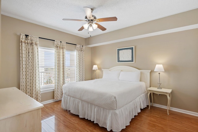 bedroom featuring a textured ceiling, light wood-type flooring, a ceiling fan, and baseboards