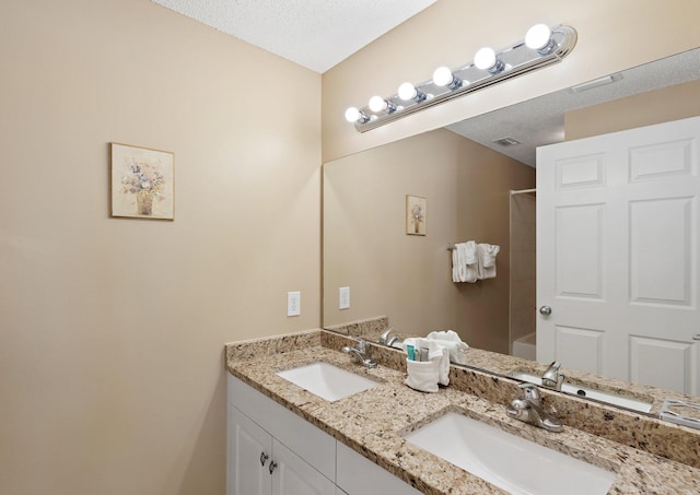 bathroom with double vanity, a textured ceiling, visible vents, and a sink