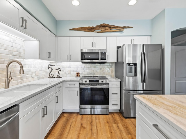 kitchen with appliances with stainless steel finishes, white cabinetry, a sink, and decorative backsplash