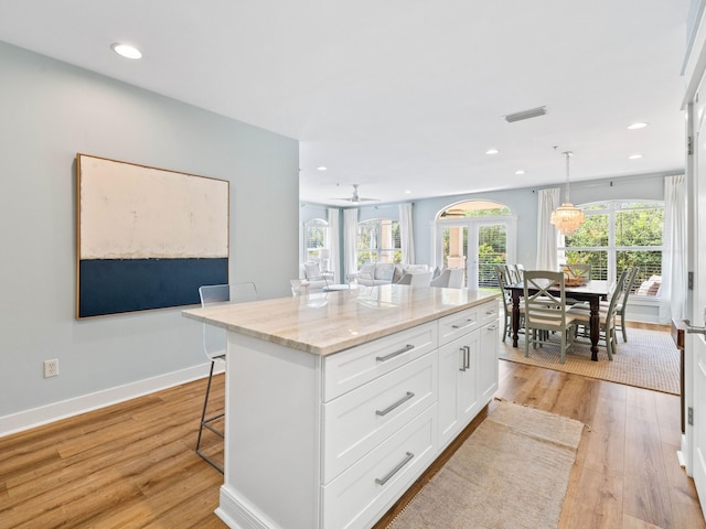 kitchen with light stone counters, visible vents, a kitchen breakfast bar, white cabinets, and light wood-type flooring