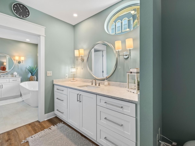 full bath with two vanities, a sink, wood finished floors, a freestanding tub, and baseboards