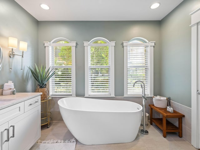 bathroom with a freestanding bath, tile patterned floors, vanity, and tile walls