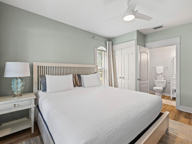 bedroom featuring wood finished floors, visible vents, baseboards, a closet, and ensuite bath