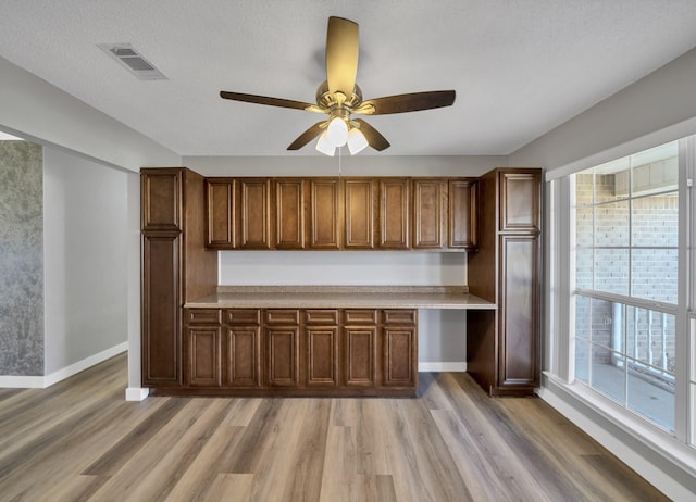 kitchen featuring light wood-style flooring, visible vents, baseboards, light countertops, and built in study area