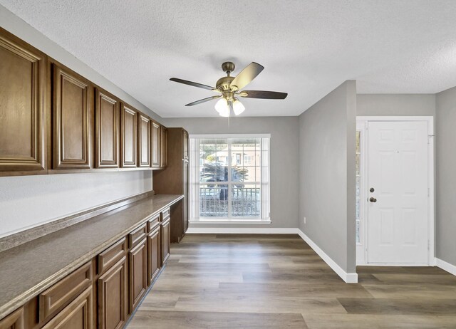 kitchen featuring dark countertops, a ceiling fan, a textured ceiling, wood finished floors, and baseboards