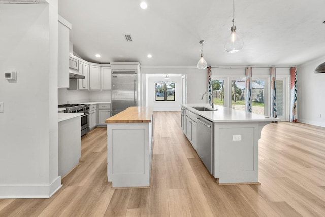 kitchen with premium appliances, an island with sink, light wood-type flooring, wooden counters, and a sink