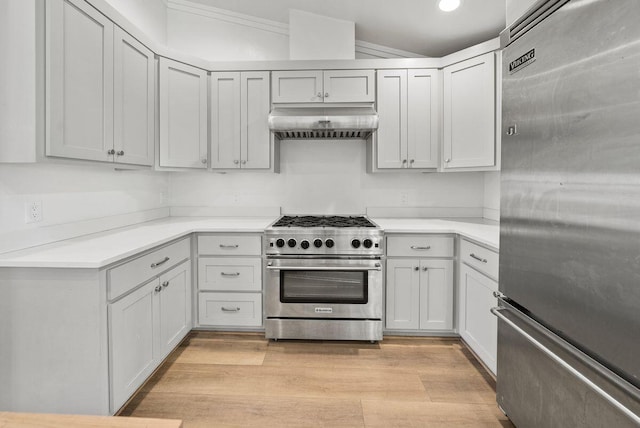 kitchen featuring high end appliances, light wood-style floors, vaulted ceiling, light countertops, and wall chimney range hood