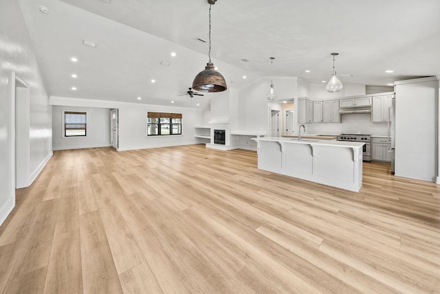 kitchen featuring stainless steel range, gray cabinetry, open floor plan, a sink, and under cabinet range hood