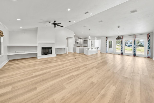 unfurnished living room with recessed lighting, a fireplace with raised hearth, visible vents, vaulted ceiling, and light wood-type flooring