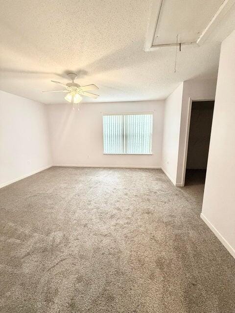 spare room with a textured ceiling, carpet floors, attic access, and baseboards