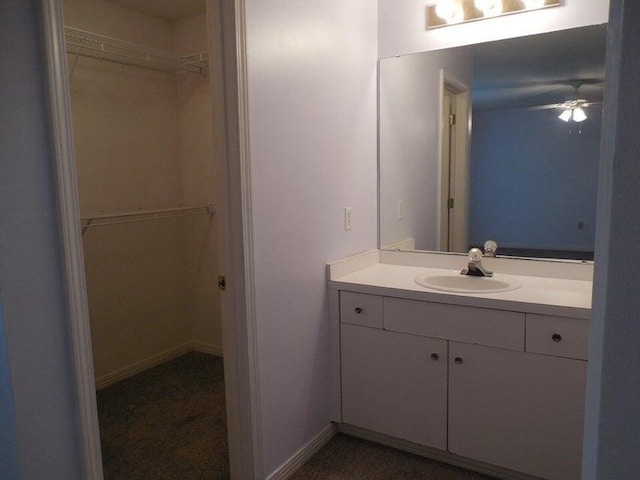 bathroom featuring a walk in closet, ceiling fan, vanity, and baseboards