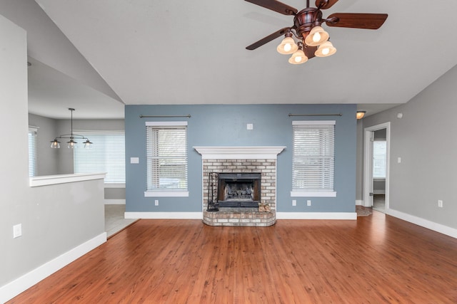 unfurnished living room featuring a fireplace, vaulted ceiling, wood finished floors, baseboards, and ceiling fan with notable chandelier