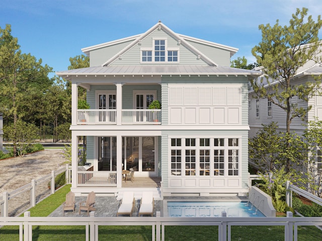 back of property with an outdoor pool, a balcony, a fenced backyard, metal roof, and a standing seam roof