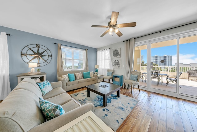 living area with a wealth of natural light, a view of city, a ceiling fan, and wood finished floors