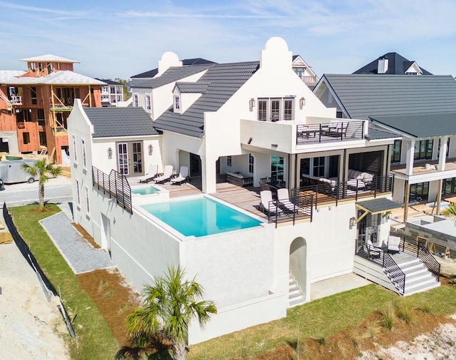 back of house with an outdoor pool, a balcony, a tile roof, a patio area, and stucco siding