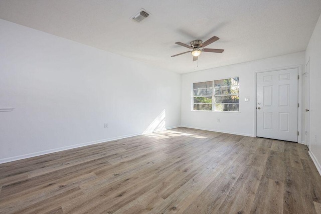 unfurnished room featuring a ceiling fan, visible vents, baseboards, and wood finished floors