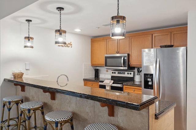 kitchen with a breakfast bar, hanging light fixtures, tile counters, decorative backsplash, and appliances with stainless steel finishes