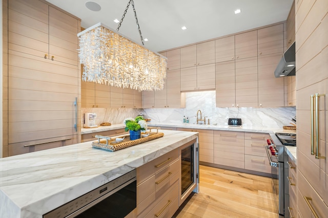 kitchen with high end stove, modern cabinets, light brown cabinetry, under cabinet range hood, and backsplash