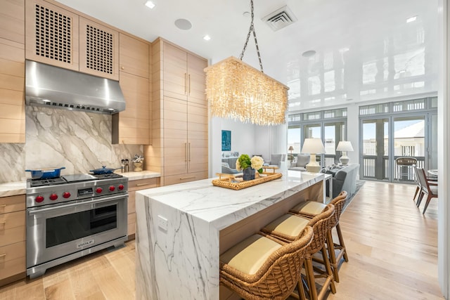 kitchen featuring visible vents, a kitchen island, under cabinet range hood, open floor plan, and premium range