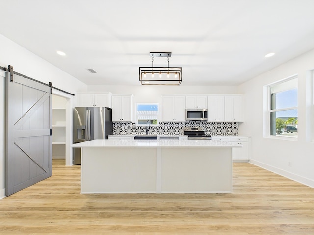 kitchen with appliances with stainless steel finishes, a barn door, backsplash, and a center island