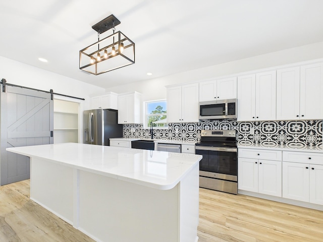 kitchen featuring a barn door, a center island, light wood-style floors, appliances with stainless steel finishes, and decorative backsplash