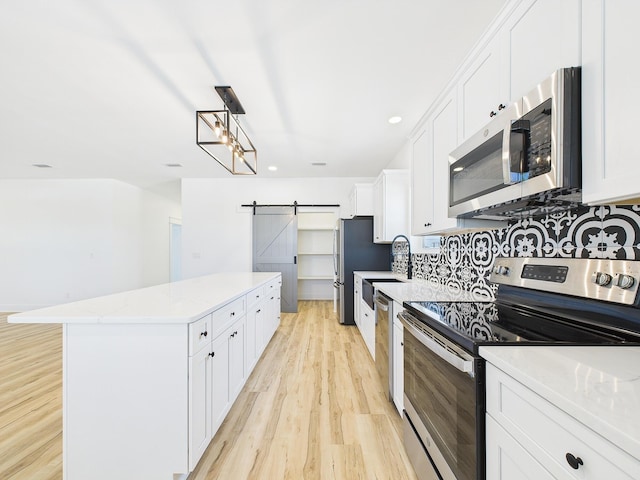 kitchen featuring light wood-style flooring, a barn door, appliances with stainless steel finishes, white cabinetry, and a kitchen island