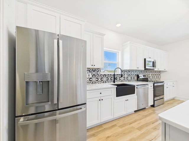 kitchen with light countertops, backsplash, appliances with stainless steel finishes, light wood-style floors, and a sink