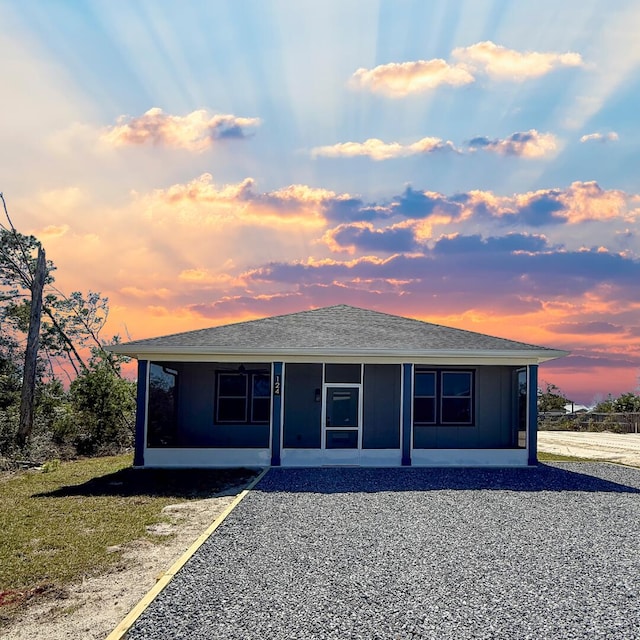 rear view of property with roof with shingles, board and batten siding, and a sunroom