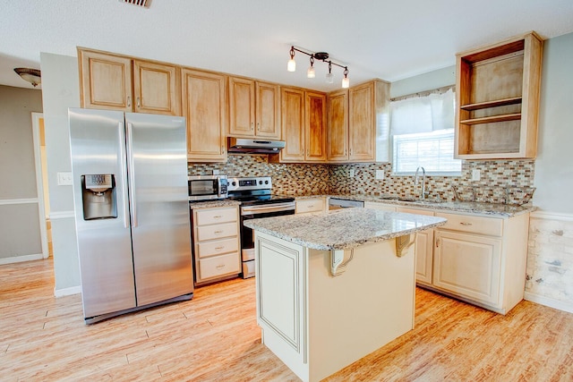 kitchen with light wood-style flooring, appliances with stainless steel finishes, light stone countertops, under cabinet range hood, and a sink