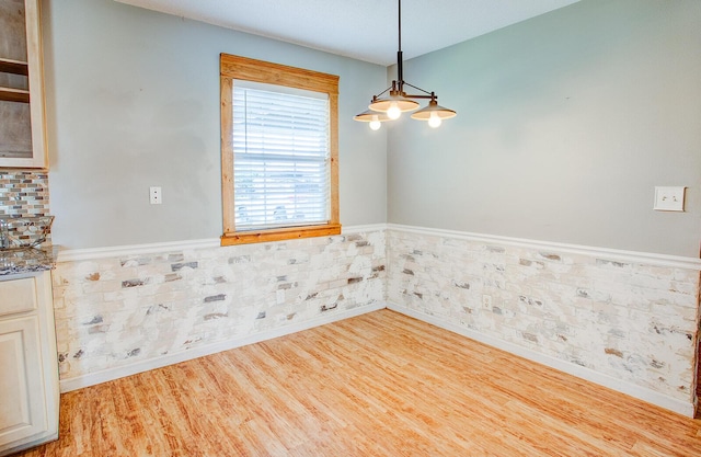 unfurnished dining area featuring a wainscoted wall and wood finished floors