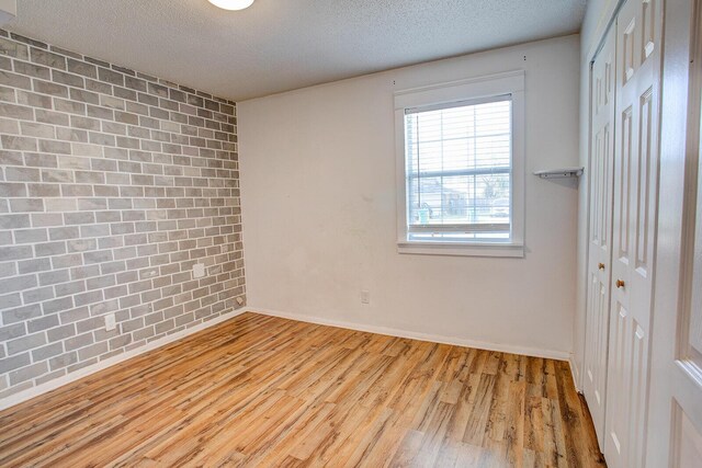 unfurnished room with a textured ceiling, brick wall, an accent wall, wood finished floors, and baseboards