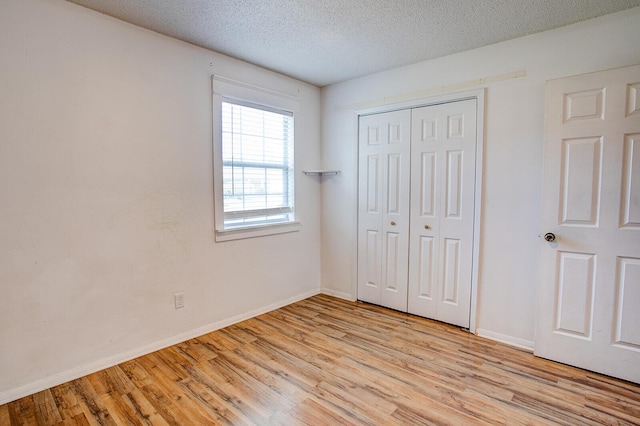 unfurnished bedroom featuring light wood finished floors, a closet, baseboards, and a textured ceiling