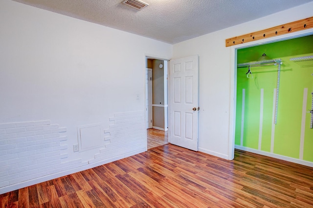 unfurnished bedroom with a textured ceiling, wood finished floors, visible vents, baseboards, and a closet