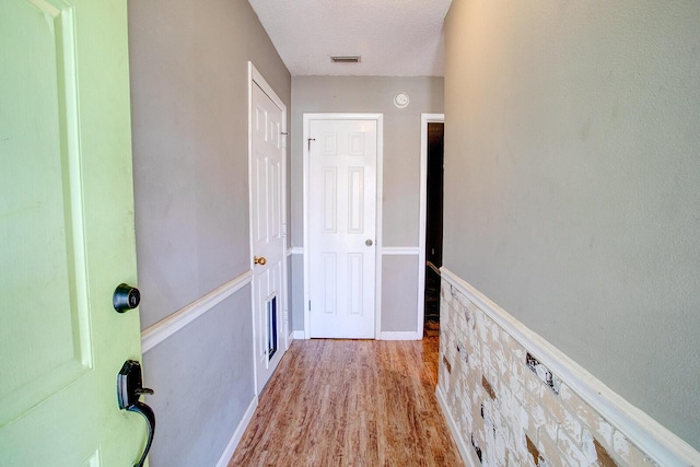 hall featuring a textured ceiling, visible vents, wood finished floors, and wainscoting