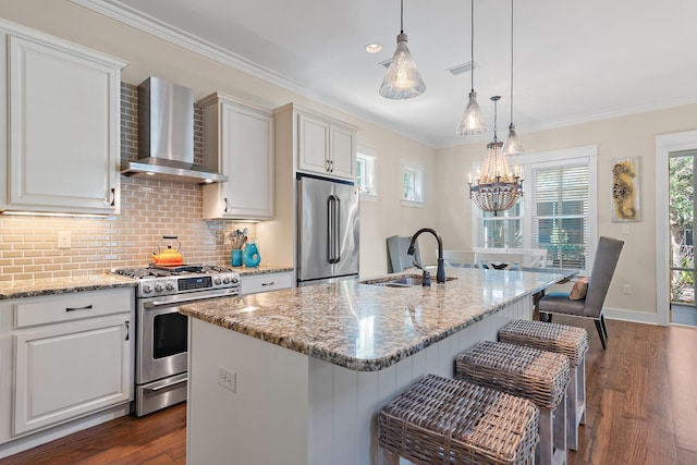 kitchen with dark wood-style flooring, a sink, ornamental molding, wall chimney range hood, and appliances with stainless steel finishes