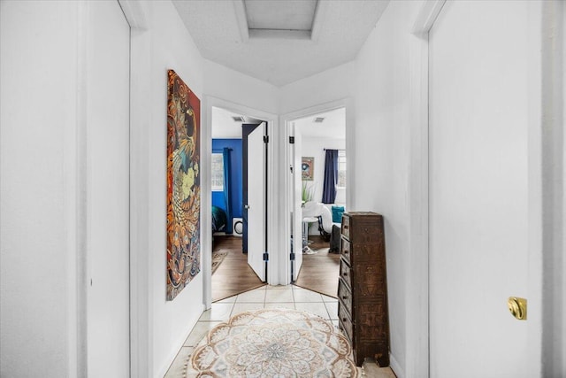 hallway featuring attic access and light tile patterned flooring