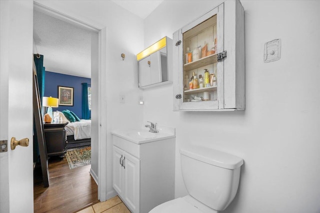 ensuite bathroom with toilet, ensuite bath, wood finished floors, and vanity