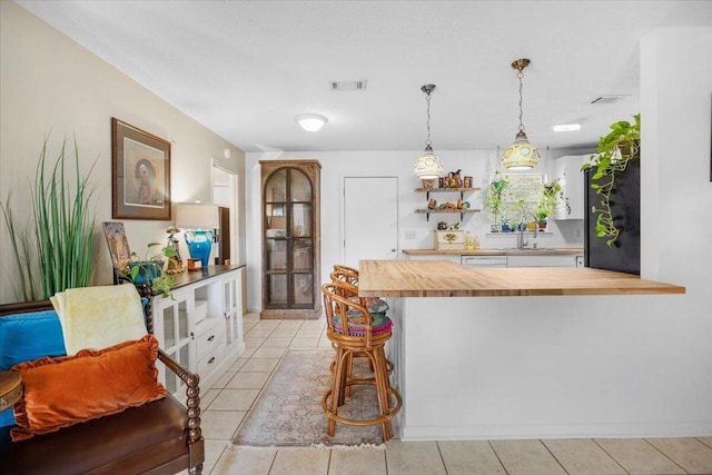 kitchen with a breakfast bar area, a peninsula, visible vents, wooden counters, and hanging light fixtures