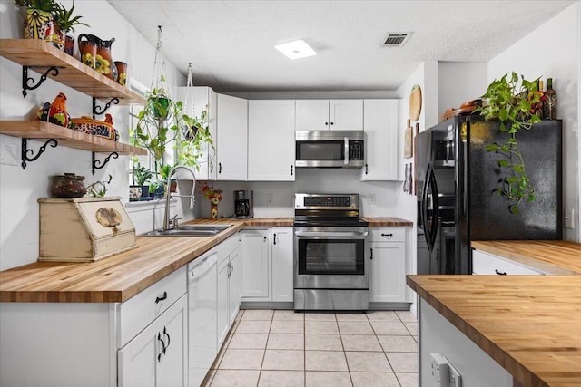 kitchen featuring light tile patterned floors, appliances with stainless steel finishes, white cabinetry, a sink, and wood counters