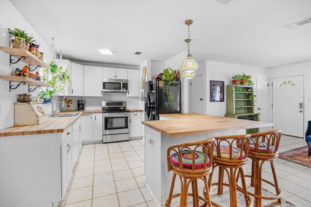 kitchen with appliances with stainless steel finishes, butcher block counters, light tile patterned flooring, and a sink