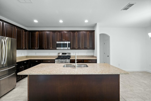 kitchen featuring visible vents, light stone countertops, dark brown cabinetry, stainless steel appliances, and a sink