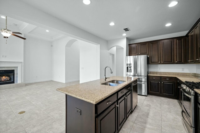 kitchen with light stone countertops, a tiled fireplace, arched walkways, stainless steel appliances, and a sink