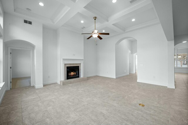 unfurnished living room with visible vents, coffered ceiling, arched walkways, a premium fireplace, and a towering ceiling