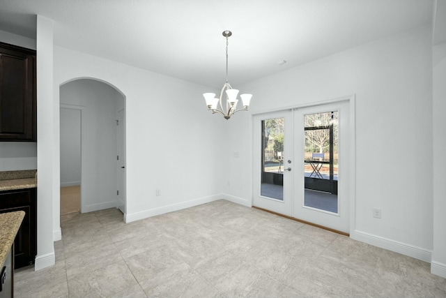 unfurnished dining area with baseboards, arched walkways, and french doors