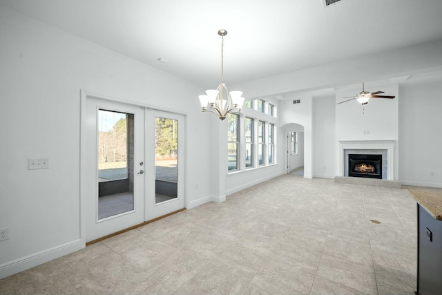 unfurnished living room featuring arched walkways, french doors, baseboards, and a lit fireplace