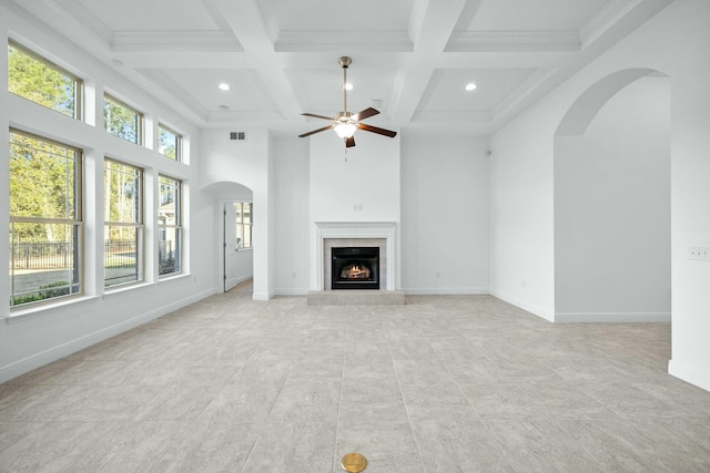 unfurnished living room with arched walkways, beamed ceiling, a fireplace, and baseboards