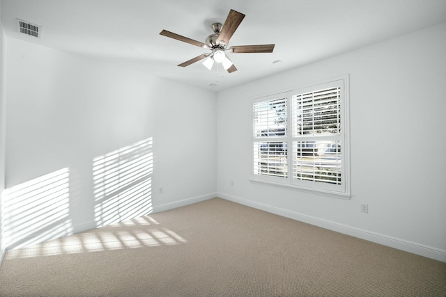 empty room with visible vents, light colored carpet, a ceiling fan, and baseboards