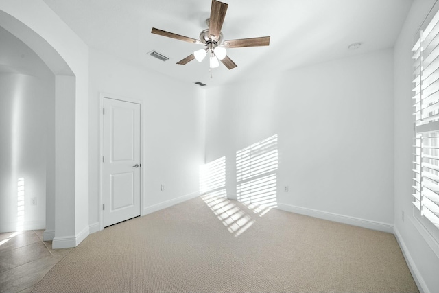 carpeted spare room featuring arched walkways, visible vents, a wealth of natural light, and baseboards